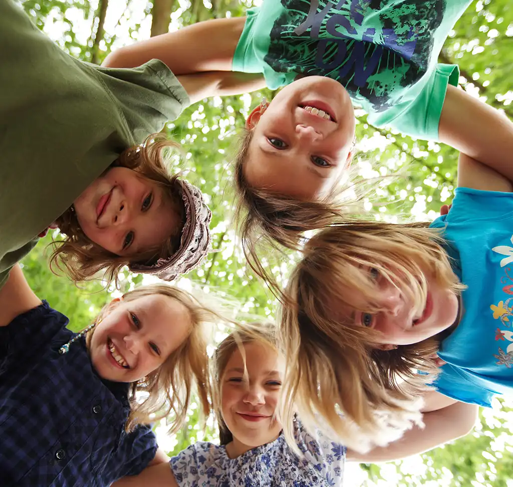 Fünf Kindergesichter, die lachend nach unten schauen.